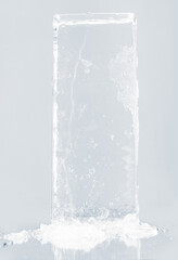 Crystal clear natural ice block in light blue tones on a white reflective surface.