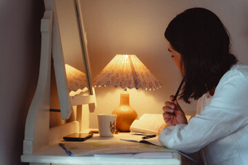 Young woman sitting at the desk of the hotel where she is staying methodically preparing the next...