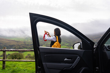Woman standing next to the road and framed by the window of her vehicle while taking a beautiful...