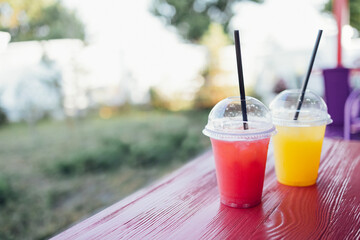 Two bright ice cocktails in plastic cups with straws on a wooden table in an open air cafe. Close up of delicious berry and citrus juices outdoors.