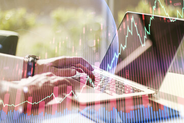 Multi exposure of abstract financial graph with world map and with hand typing on laptop on background, financial and trading concept
