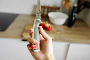 Woman cut her little finger with a knife while cooking vegetable salad on the kitchen. Female hand with blood holds knife with a sharp blade resulted in a cut and wounded finger cooking accident.