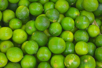 Fresh green ripe lime fruits on retail market stall display, close up view. 