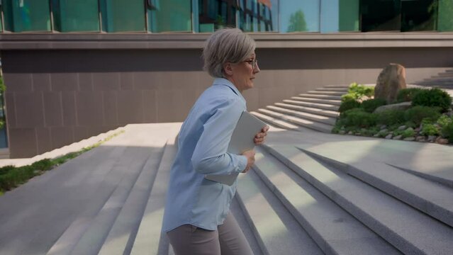 Caucasian mature business woman hurries walking up stairs office building in city looking at hand watch busy senior adult businesswoman female employer running fast to work with folder lateness time