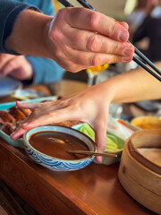Obraz premium woman's hand and man's hand with chopsticks preparing a duck roll served Asian-style with vegetables and sauce