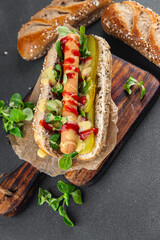 Hot Dog sausage on bun, tomato sauce, pickled cucumber, greens lettuce leaf takeaway food tasty fresh eating cooking appetizer meal food snack on the table