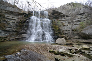 A stunning waterfall cascades over rocky cliffs, surrounded by lush greenery, creating a serene, picturesque natural scene
