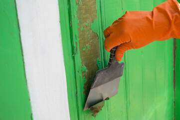 Cleaning the door facade from green paint using an old wide trowel. Removing the coating using a construction tool. Household repairs. Selective focus. Copy space