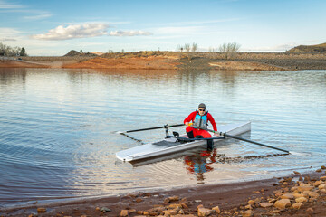Senior male rower in a coastal rowing shell is landing on a rocky shore of Horsetooth Reservoir in...