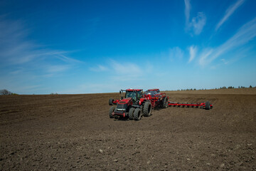 Red tractor with a planter sowing corn in the field