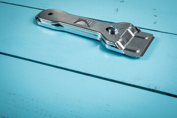 Glass ceramic scraper on a blue wooden texture background.