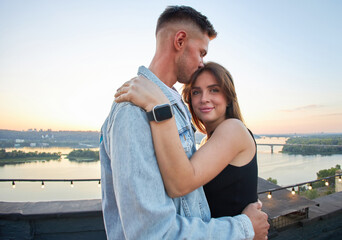 A young couple enjoys a serene evening on a rooftop, surrounded by the warm hues of a setting sun.