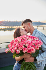 A young couple, perched on a rooftop, shares a blissful moment as the man gifts an enormous bouquet of roses