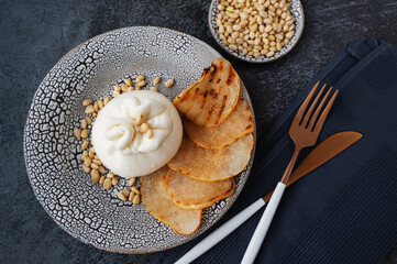burrata is served with roasted caramelized pear and pine nuts. Top view, flat lay