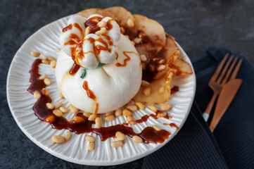 burrata is served with roasted caramelized pear and pine nuts. Close-up.