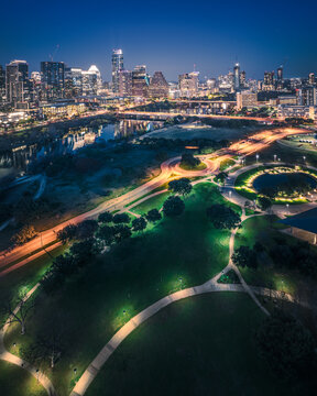 Austin skyline captured post-sunset from a drone perspective. Lady Bird Lake reflects city lights, showcasing dynamic urban charm. Aerial view of iconic landmarks and vibrant cityscape, perfect for cr