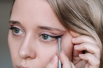 Close up of a young caucasian blonde woman using a contour brush while drawing arrows on the...