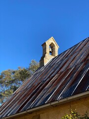 Old church steeple against blue sky. Ancient holy church. Bell tower and iron roof of an old village church.