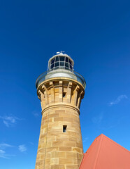 Lighthouse on the island at daytime. Sandstone lighthouse at the top of a hill. Coast lighthouse against a blue sky in the harbor. Lighthouse on the coast of the region sea.