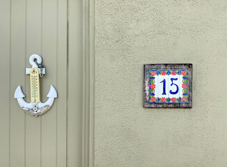 Fifteen. Number fifteen on a wall and an anchor-shaped external thermometer. Address made with ceramic tiles with red rose pattern on a house wall. Concept of the number 15. Sign and symbol, font.