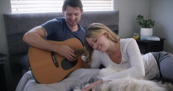 Couple, home and play guitar with dog for love and bonding, happiness in bed with pet. People with domestic animal, husky and musical instrument, time together with trust, commitment and creativity
