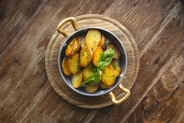 Country potatoes, fried potato slices in a frying pan on a wooden background.
