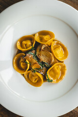 Appetizing ravioli with mushrooms in a large white plate on a wooden background.