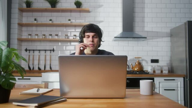 Young man sitting in kitchen at home wear wireless headset with microphone having video conference calling on laptop computer talk by webcam, learning study with online tutor
