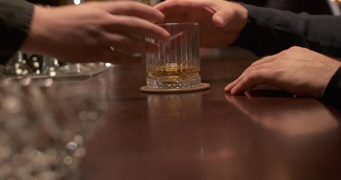 The bartender pushes a glass of whiskey on the counter to the customer. Bar or pub in the evening