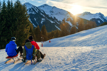 Friends ready for sledding against a sunset backdrop in the Alps, capturing a popular winter holiday activity in nature the mountain's tranquil beauty, a serene moment before an exhilarating descent - obrazy, fototapety, plakaty