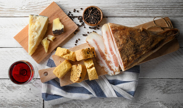 Savory biscuit with pecorino, guanciale and pepper. Cutting board with Italian rustic snack and red wine glass on white wooden background. close-up.