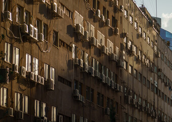 Sunlight bathes an apartment facade dotted with air conditioning units, casting dynamic shadows.