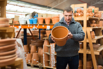 Portrait of focused greenhouse owner choosing plant pots in garden material warehouse