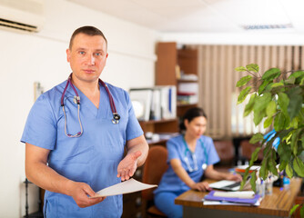 Obraz premium Positive doctor standing in office with clipboard, holding medical history sheet