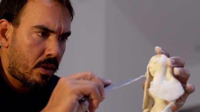 Explore the cultural precision as a Latino sculptor expertly refines the figure's hair using a small knife.