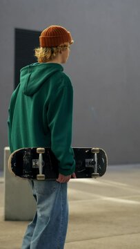 Rear view of holding skateboard walking at urban place