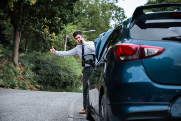 Asian businessman standing by broken car with warning triangle and calling for help. Man waiting for roadside assistance. Reproach and blame concept in transportation and travel. - obrazy, fototapety, plakaty