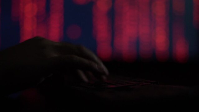 Hands of a cybercriminal working with a computer keyboard. On a red background
