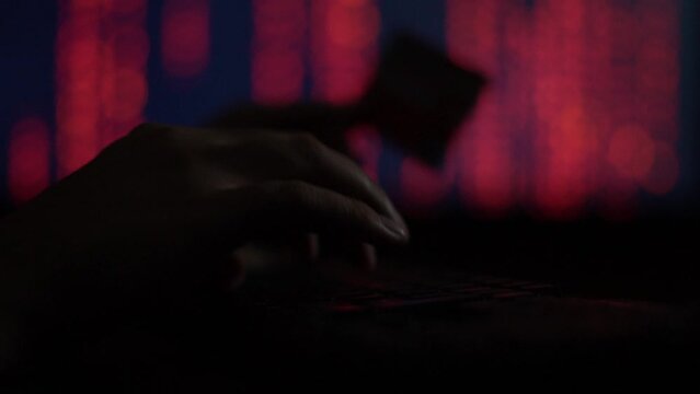 Hands of a cybercriminal working with a computer keyboard. On a red background