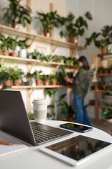 Naklejka na ściany i meble Electronic devices displayed on desk in plant store, worker arranging plants on background