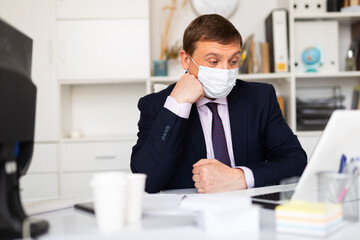 Portrait of pensive businessman in medical facial mask working in office. Concept of health...