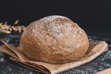 Round white bread on a paper bag on a black table.