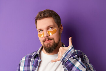 Man in white tshirt with eye patches stand against violet background. Beauty treatment spa...