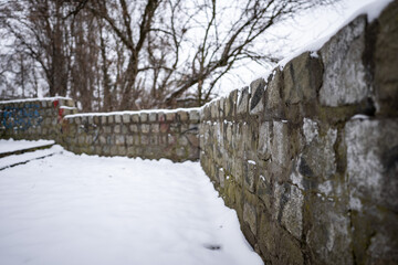 Zbliżenie na uciekający w dal kamienny murek pokryty śniegiem o zimowej porze roku w pochmurny...