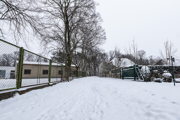 Fototapeta na wymiar Śnieżna ścieżka idąca między posesjami odgrodzonymi płotami z siatki w zachodniej Polsce o wieczornej porze przy dużym zachmurzeniu