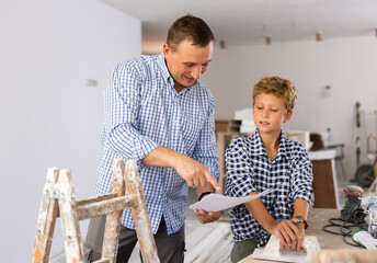 Young boy having conversation with his father about home improvement works in new apartment. Father and son looking at document.