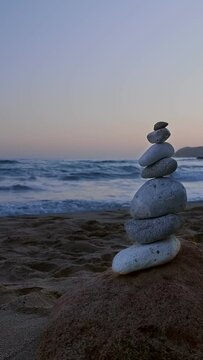 Balance stones stack on beach at sunset. Rock and sea waves in background.