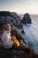 A woman looks out over the Atlantic Ocean while sitting on the rocks, Sintra, Portugal.