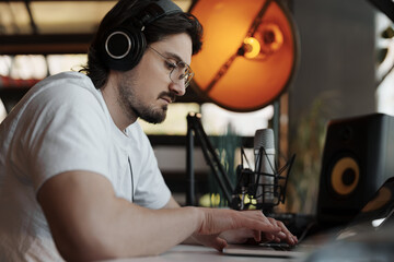 With meticulous care, an audio specialist edits music on his laptop in a studio, surrounded by...