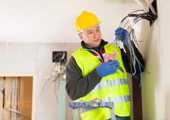 Experienced diligent electrician laying electric wires in building under construction
